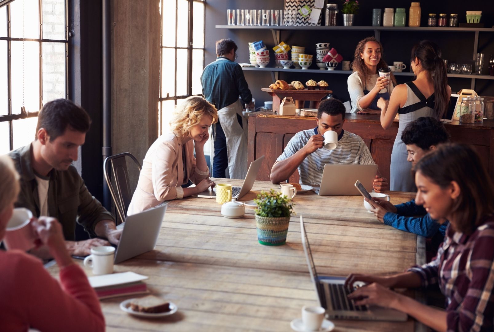 People using laptops and smartphones in a busy café with guest Wi-Fi, illustrating Wi-Fi monetization strategies for U.S. businesses